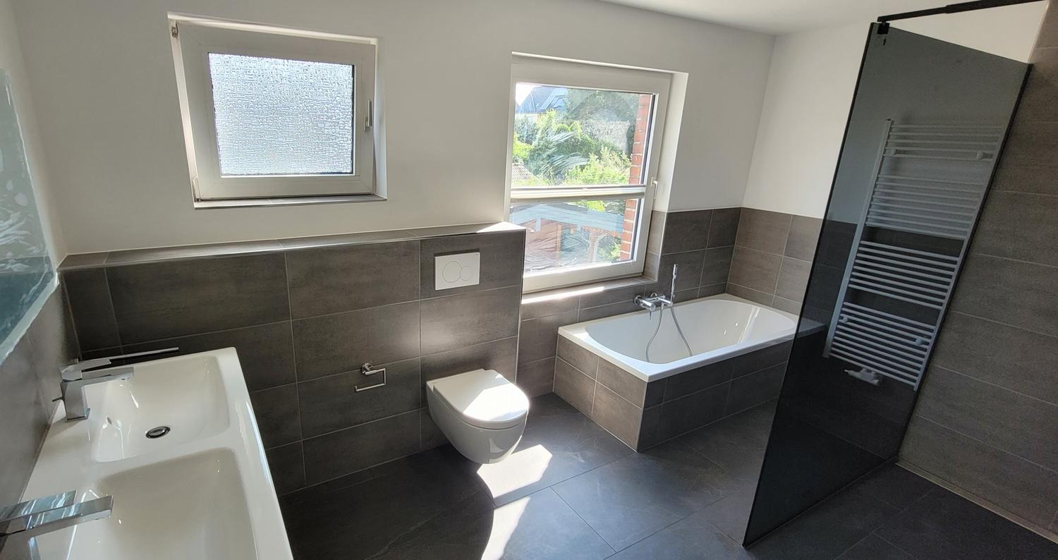 Bad mit dunklen Wandfliesen, Wand-WC, Badewanne und Duschwand