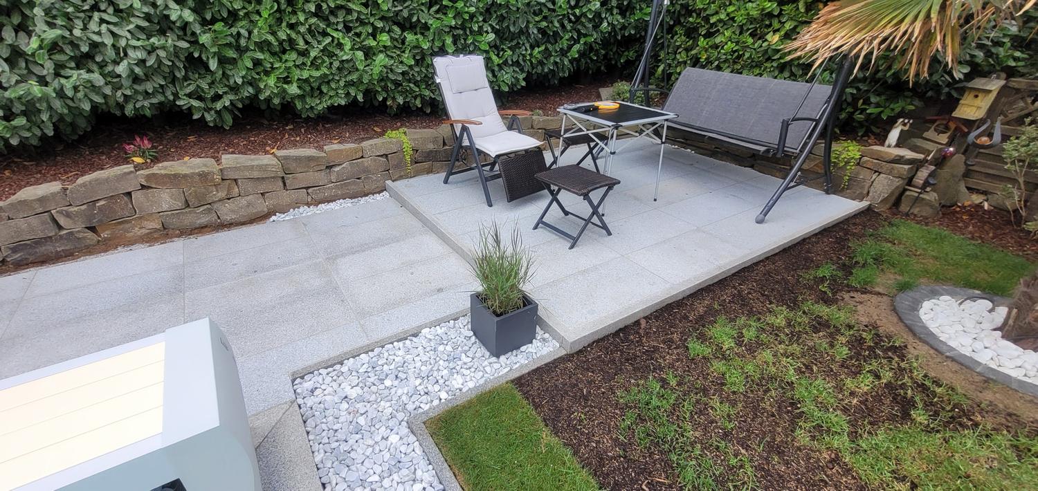 Sitzplatz im Garten mit hellen Platten, Kiesstreifen und Natursteinmauer