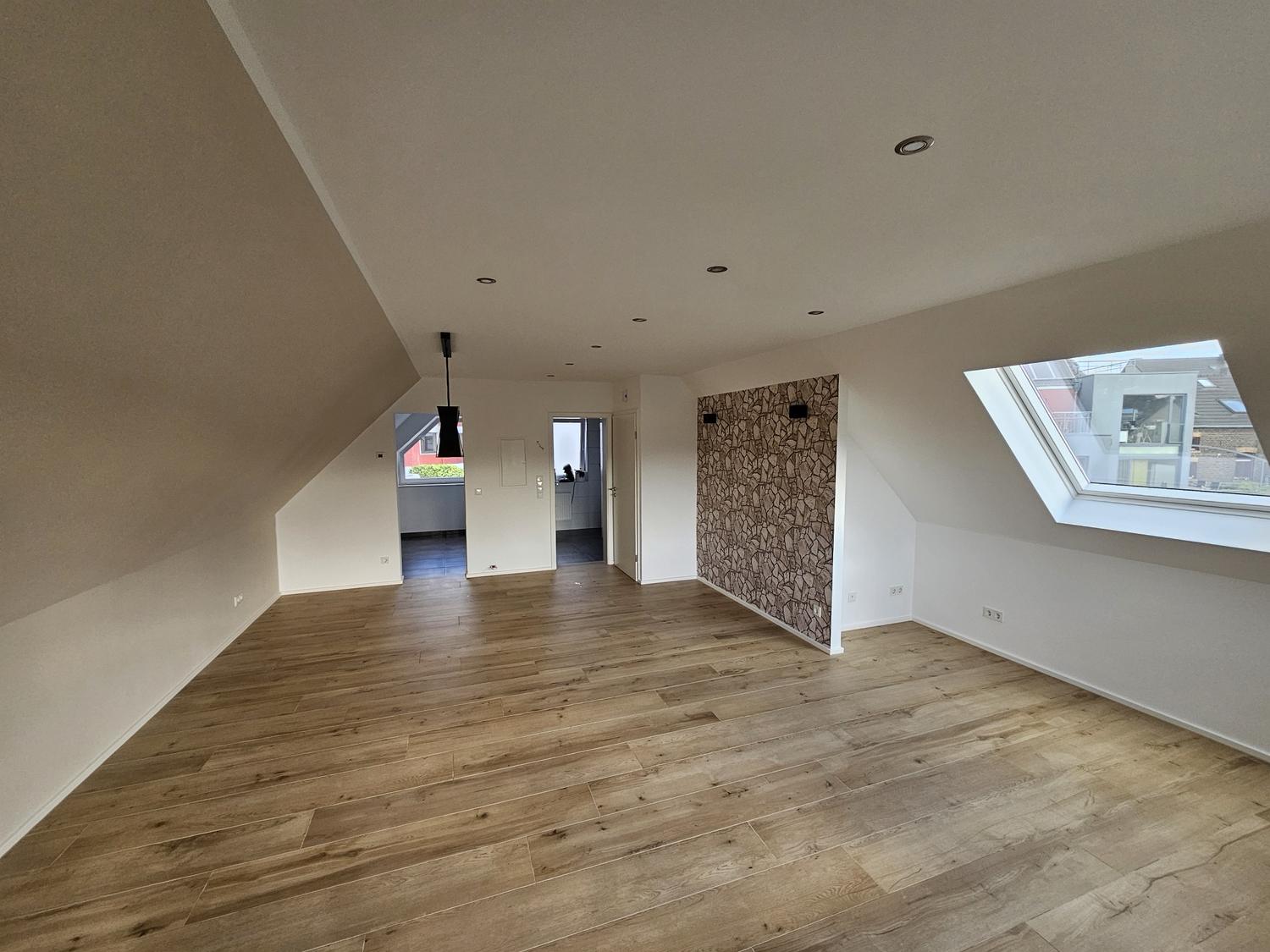 Wohnraum im Dachgeschoss mit Boden in Holzoptik, Blick zu Bad und Küche